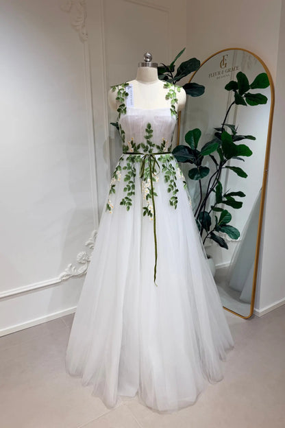 Ivory A-line tulle wedding gown with green meadow daisy embroidery, sweetheart bodice, and a thin green waist belt.