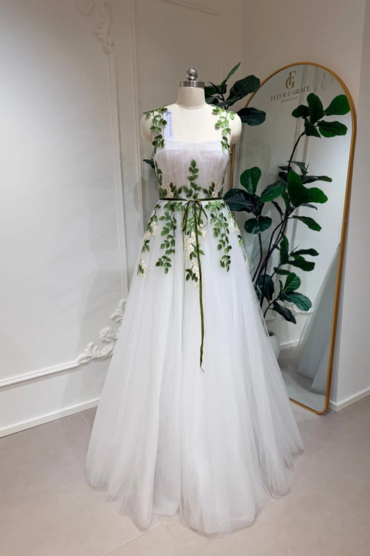 Ivory A-line tulle wedding gown with green meadow daisy embroidery, sweetheart bodice, and a thin green waist belt.