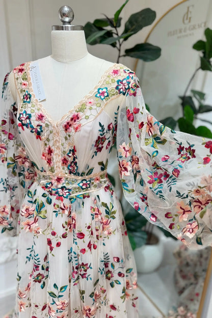 Whimsical A-line wedding dress with colorful floral embroidery, long puff sleeves, and tulle on a mannequin.