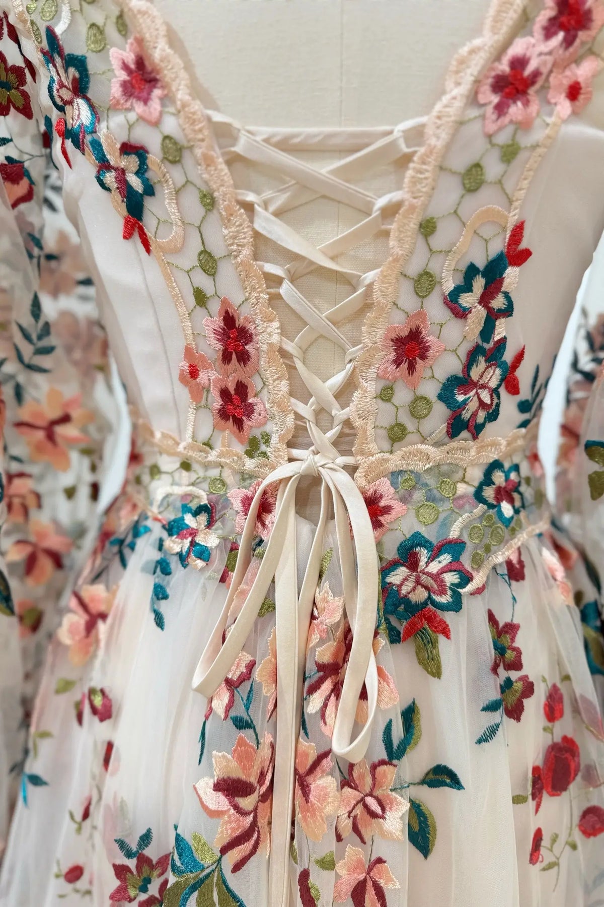 Whimsical wedding dress with pink and burgundy floral embroidery, sheer tulle, and a lace-up corset back.