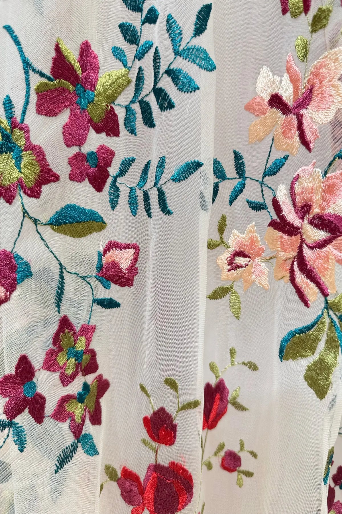 Sheer white tulle fabric with vibrant pink, burgundy, and green floral embroidery for a whimsical wedding gown.