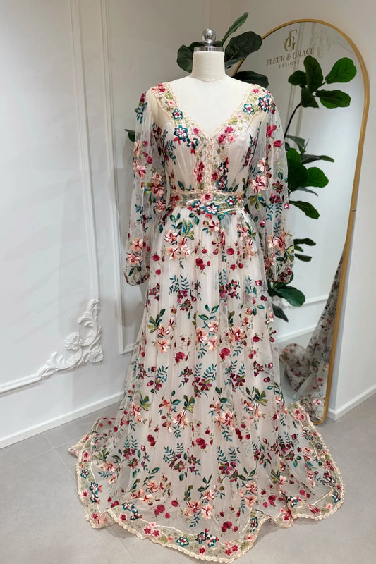 A-line wedding dress with pink and burgundy floral embroidery, long puff sleeves, and a sweep train on a mannequin.