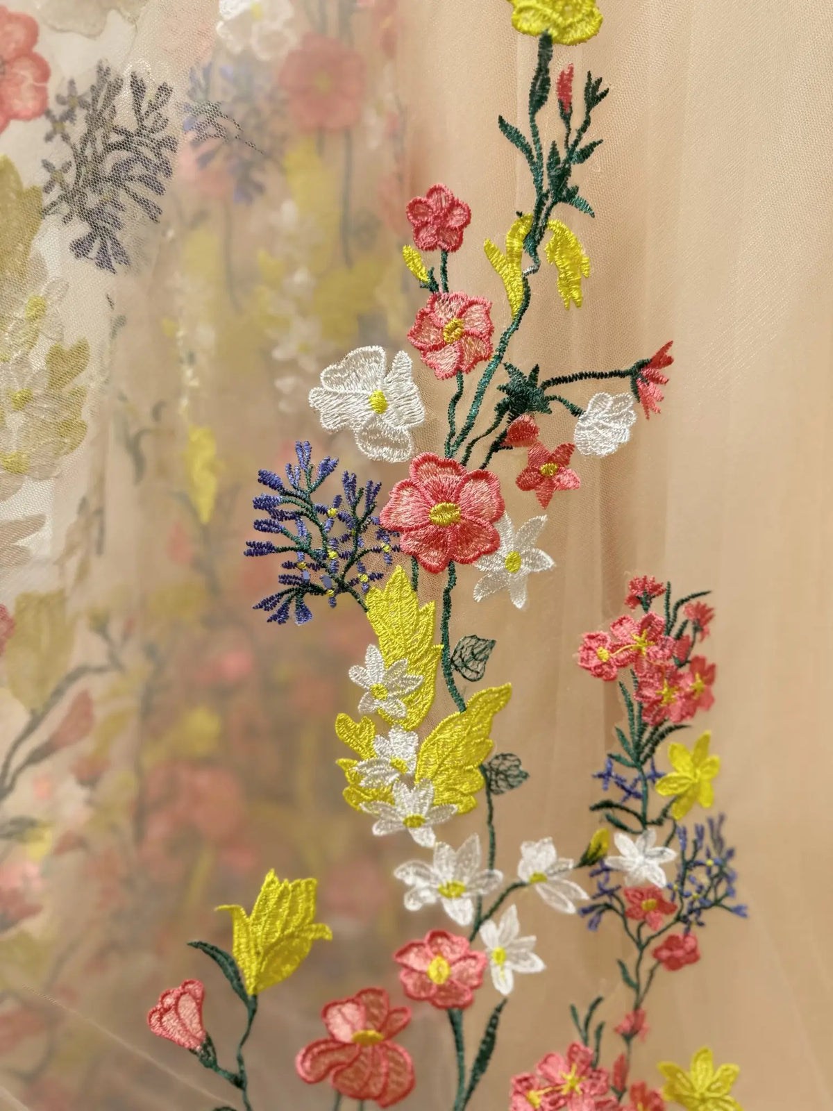 Close-up of vibrant multicolor floral embroidery on soft champagne tulle fabric for a bridal gown.