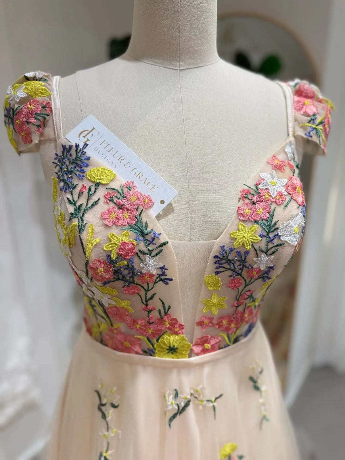 Champagne A-line wedding dress with cap sleeves and colorful floral embroidery on an illusion corset bodice.