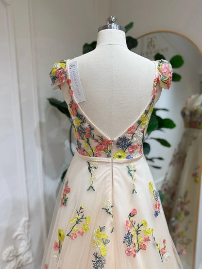 Champagne A-line wedding dress with colorful floral embroidery, cap sleeves, and a low V-back on a mannequin.