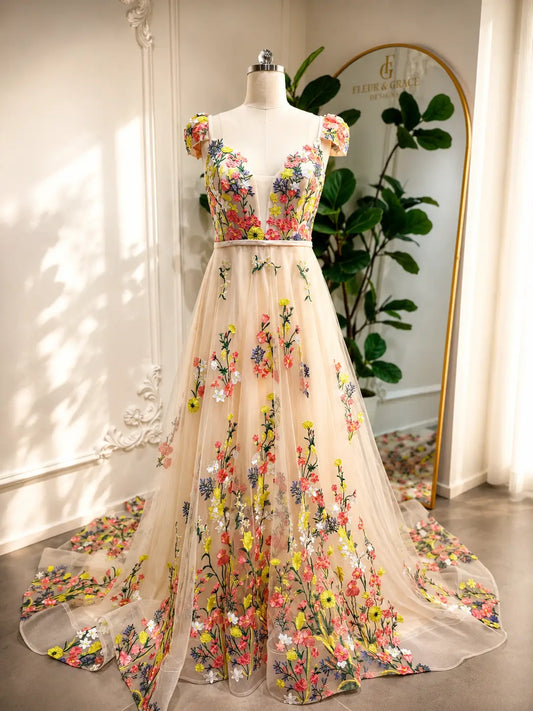 Champagne A-line wedding dress with colorful floral embroidery, illusion bodice, and cap sleeves on a mannequin.