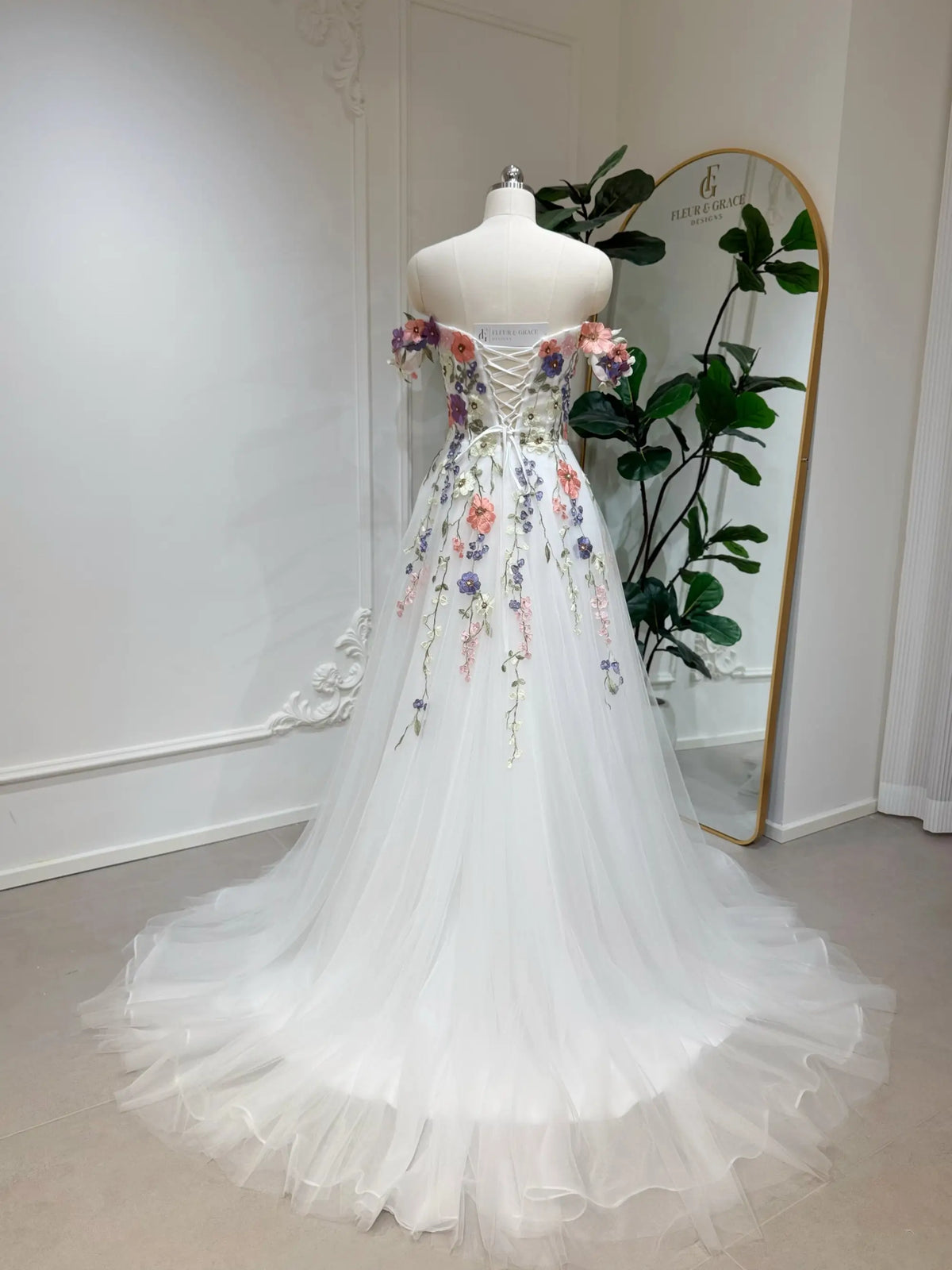 Off-shoulder A-line wedding dress with colorful 3D floral appliqué, lace-up corset back, and flowing tulle skirt.