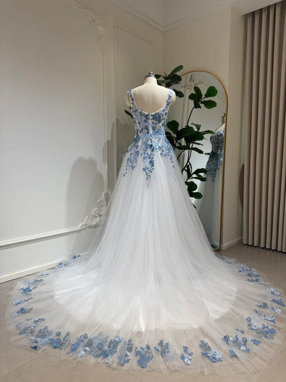 White tulle wedding gown with dusty blue floral embroidery, square neckline, and a long, detailed train on a mannequin.