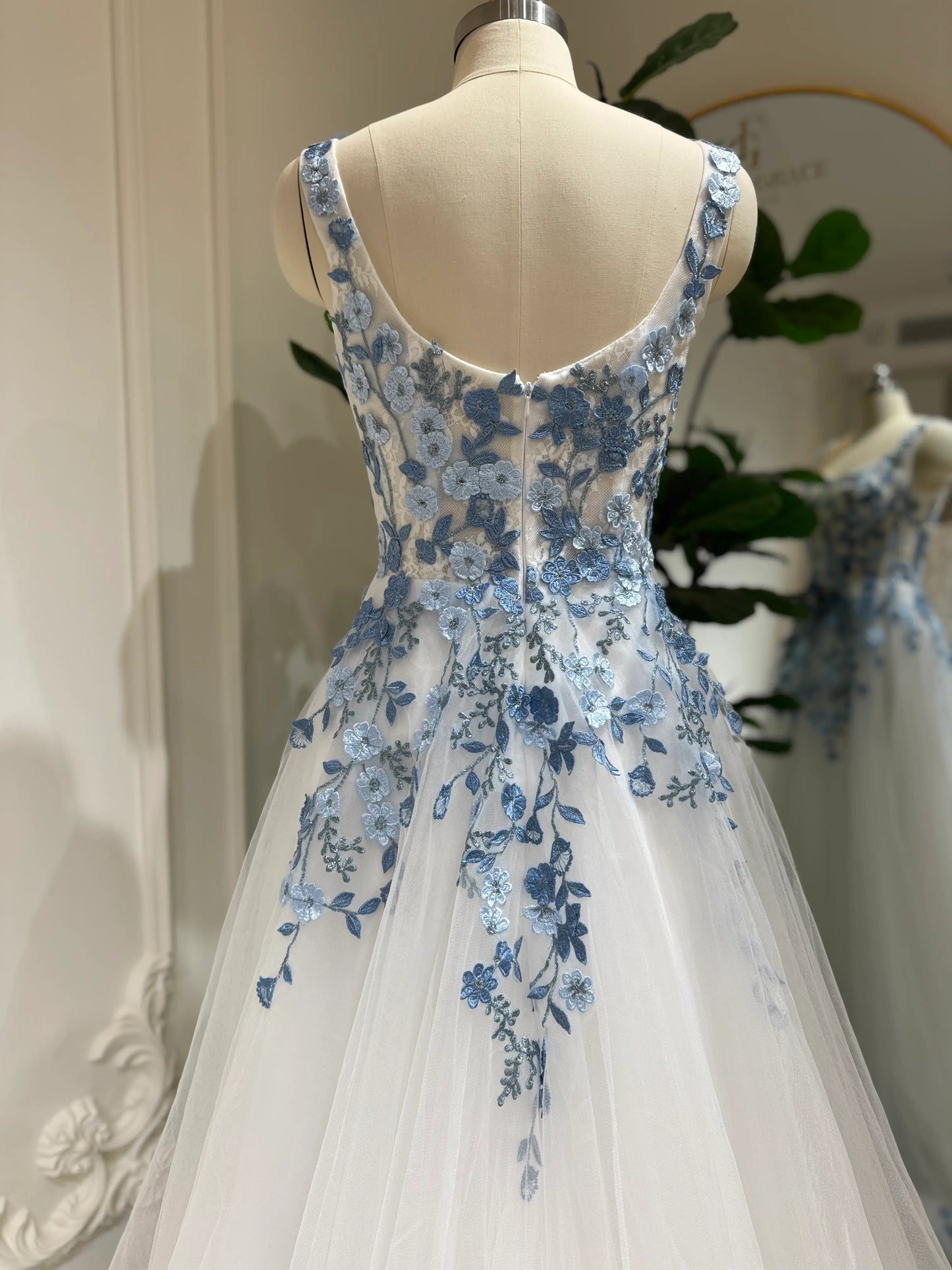 White tulle wedding gown featuring intricate dusty blue floral embroidery, a square neckline, and a structured bodice.