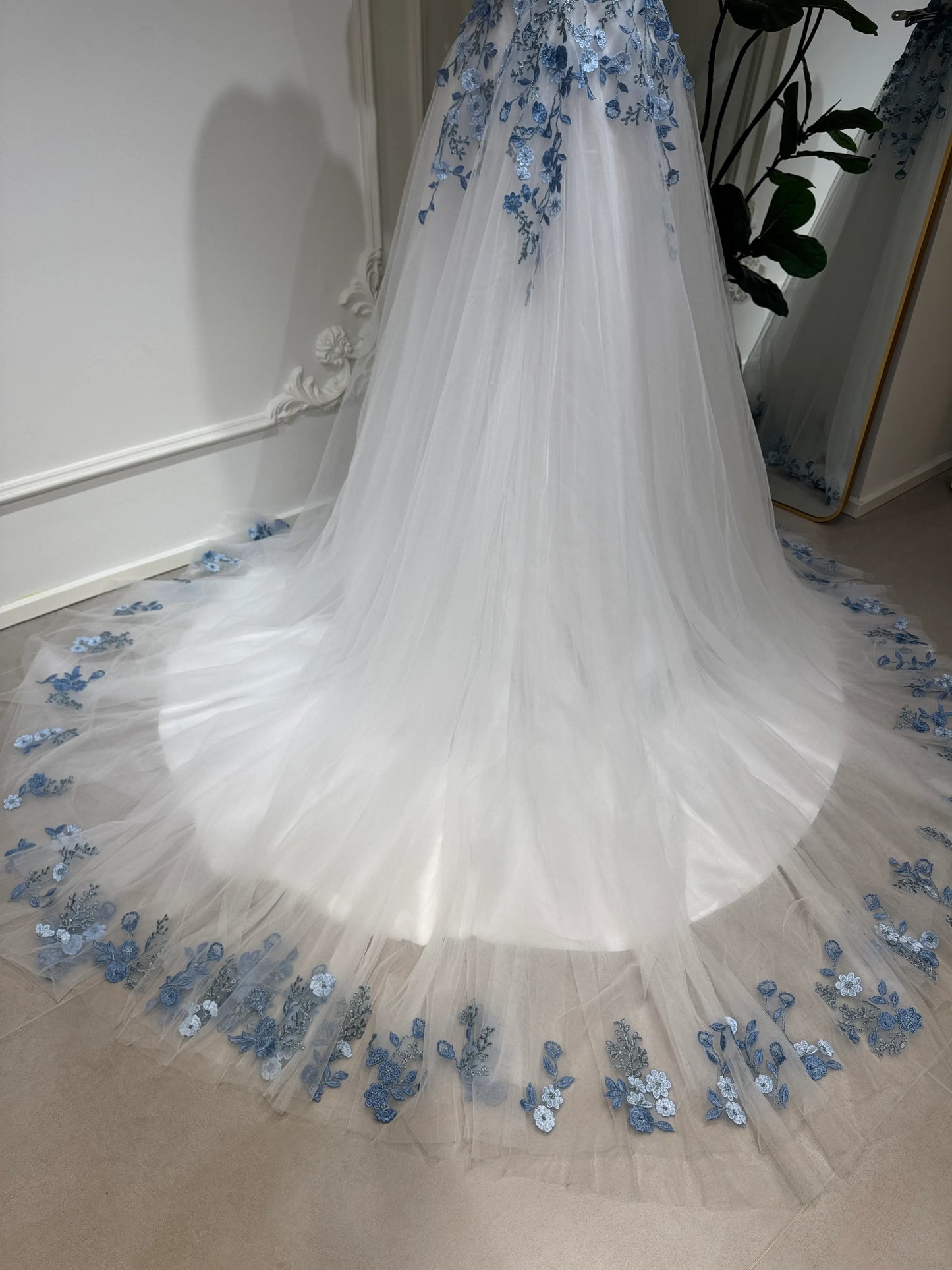 White tulle wedding gown with dusty blue floral embroidery on a chapel-length train and hem.