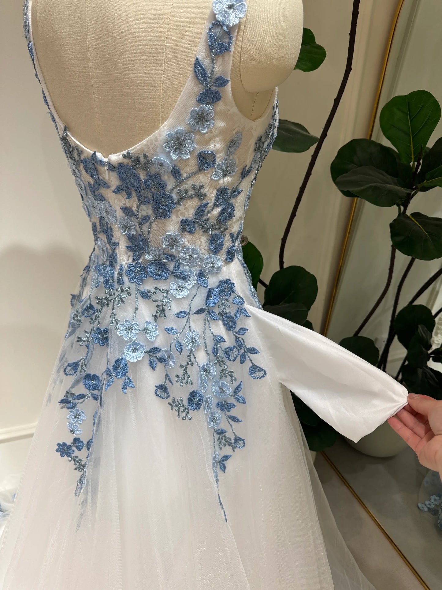 White tulle wedding gown with dusty blue floral embroidery, square neckline, and a functional side pocket.