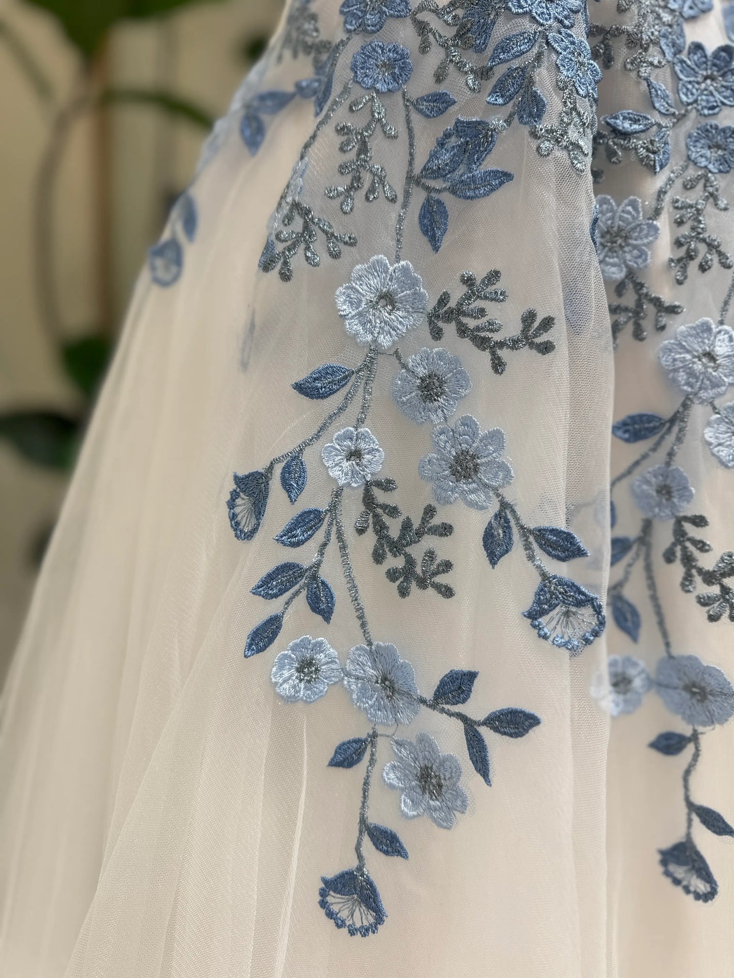 White tulle wedding gown featuring delicate dusty blue floral embroidery and intricate vine details.
