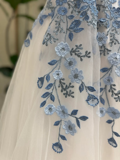 White tulle wedding gown featuring delicate dusty blue floral embroidery and intricate vine details.