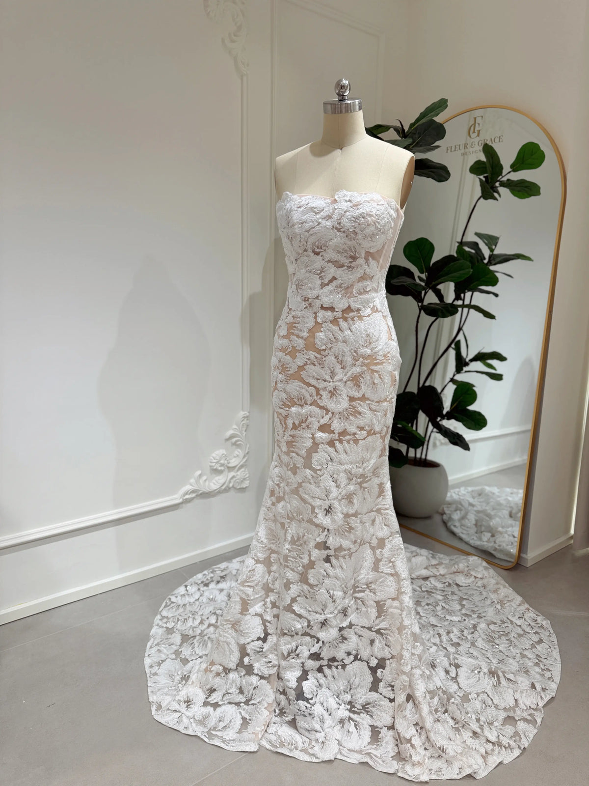 Strapless mermaid wedding dress with floral embroidered lace, glitter sequins, and a chapel-length train on a mannequin.