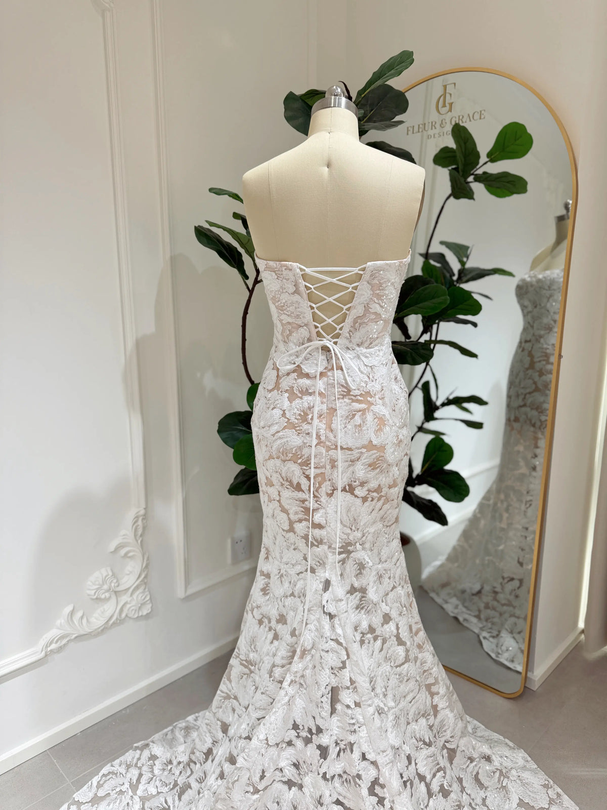 Strapless mermaid wedding dress with white floral embroidery, glitter sequins, and a lace-up corset back on a mannequin.