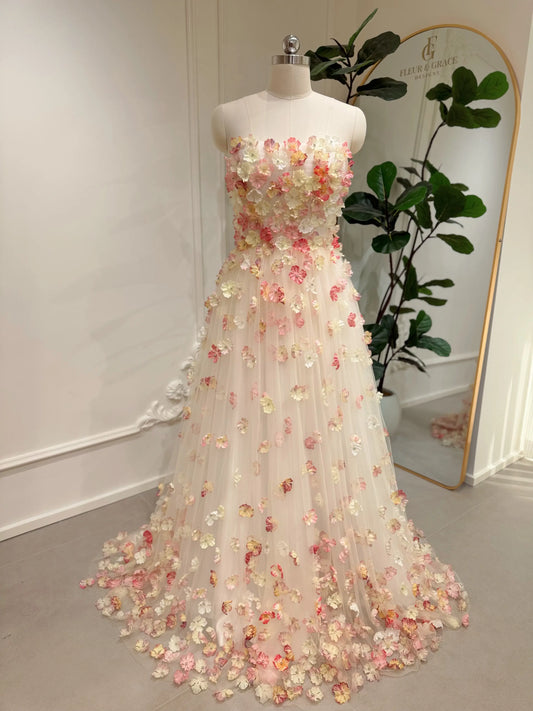 Strapless pink floor-length gown featuring 3D floral appliqués on a structured bodice and tulle skirt on a mannequin.