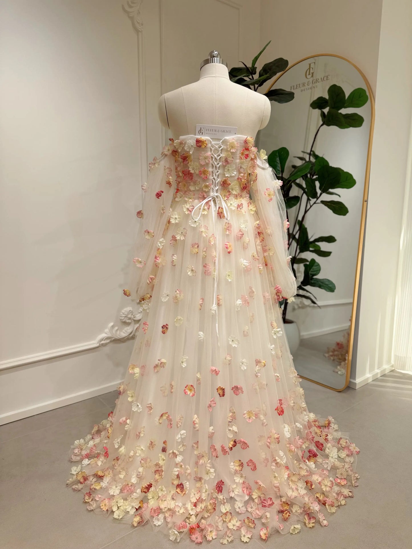 Pink floor-length wedding gown with 3D floral appliqués, removable sleeves, and a lace-up back on a dress form.