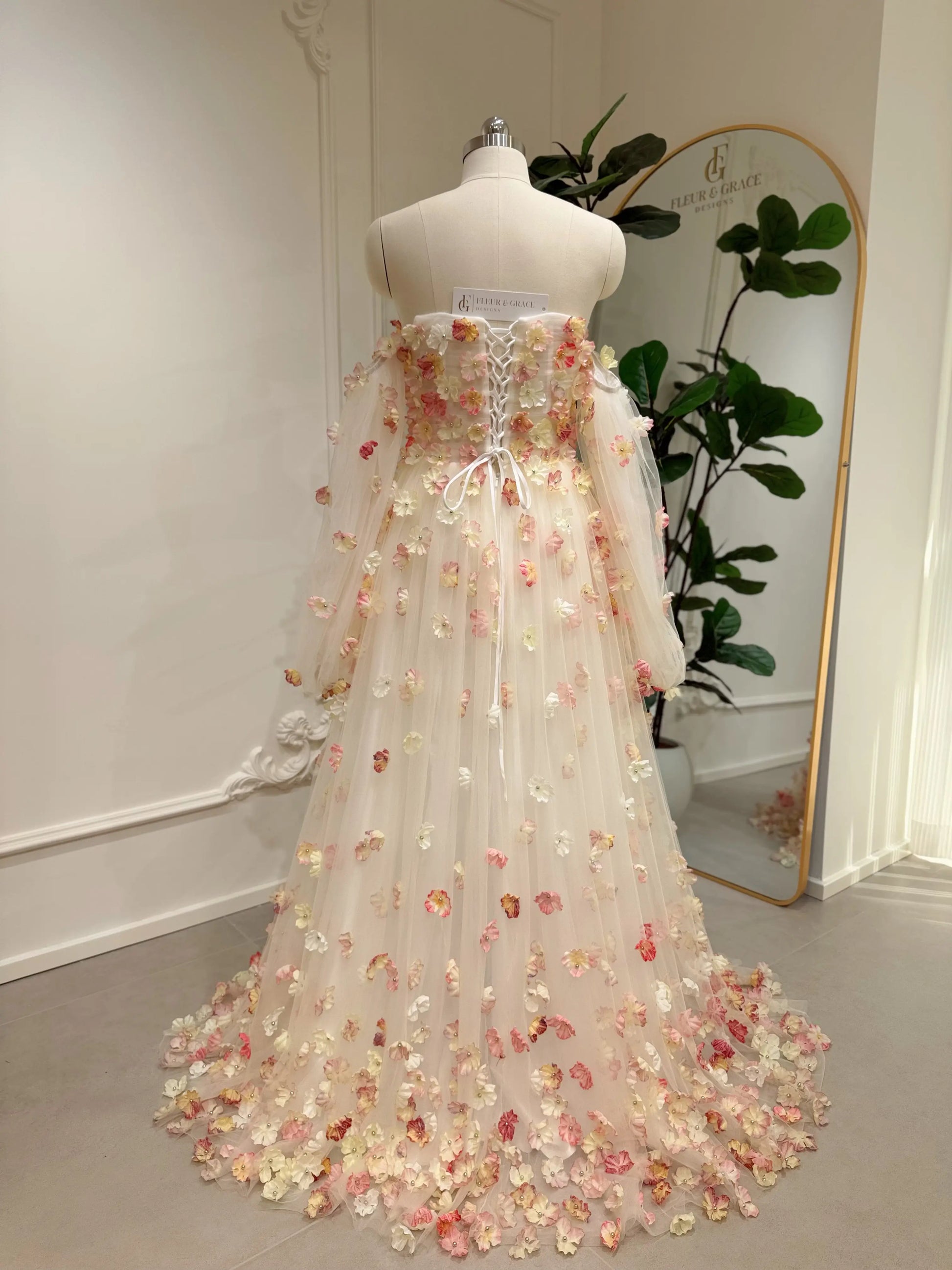Pink floor-length wedding gown with 3D floral appliqués, removable sleeves, and a lace-up back on a dress form.