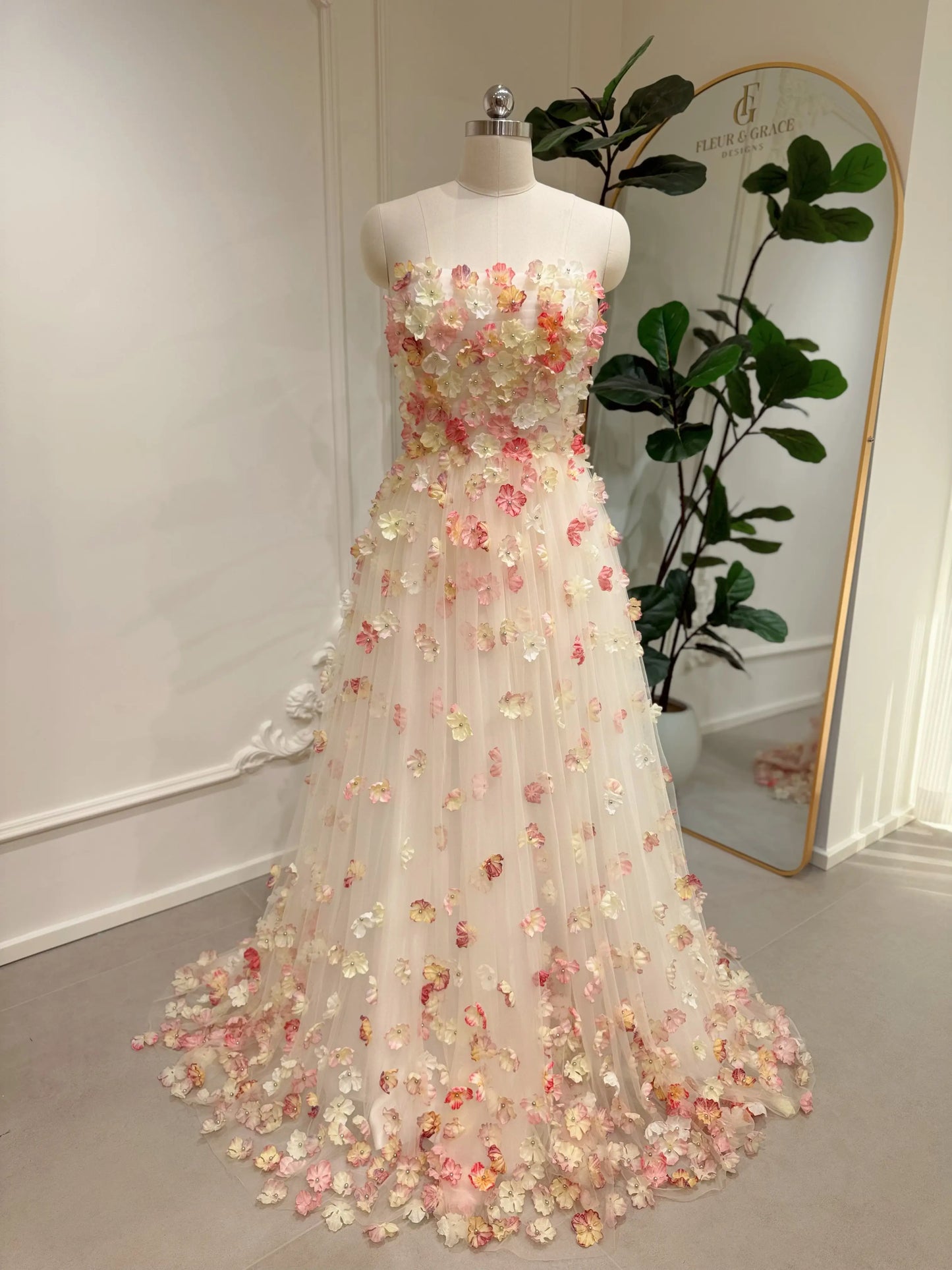 Pink strapless floor-length wedding gown featuring 3D floral appliqués on a structured bodice and tulle skirt.