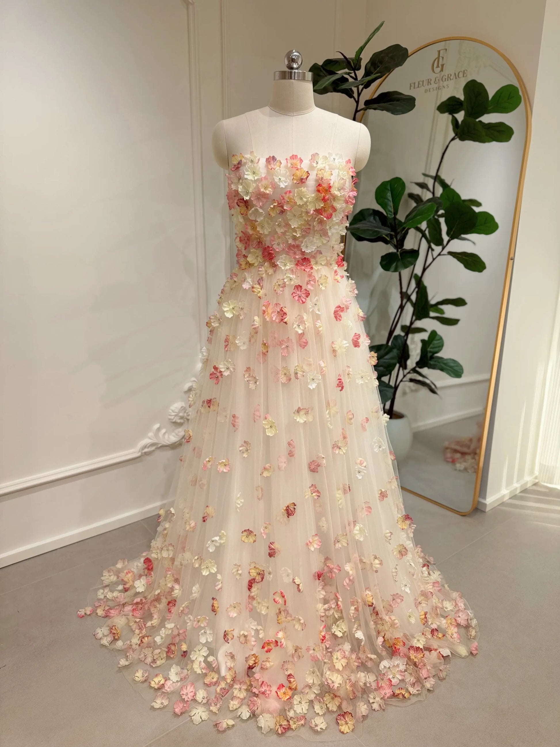 Pink strapless floor-length wedding gown featuring 3D floral appliqués on a structured bodice and tulle skirt.