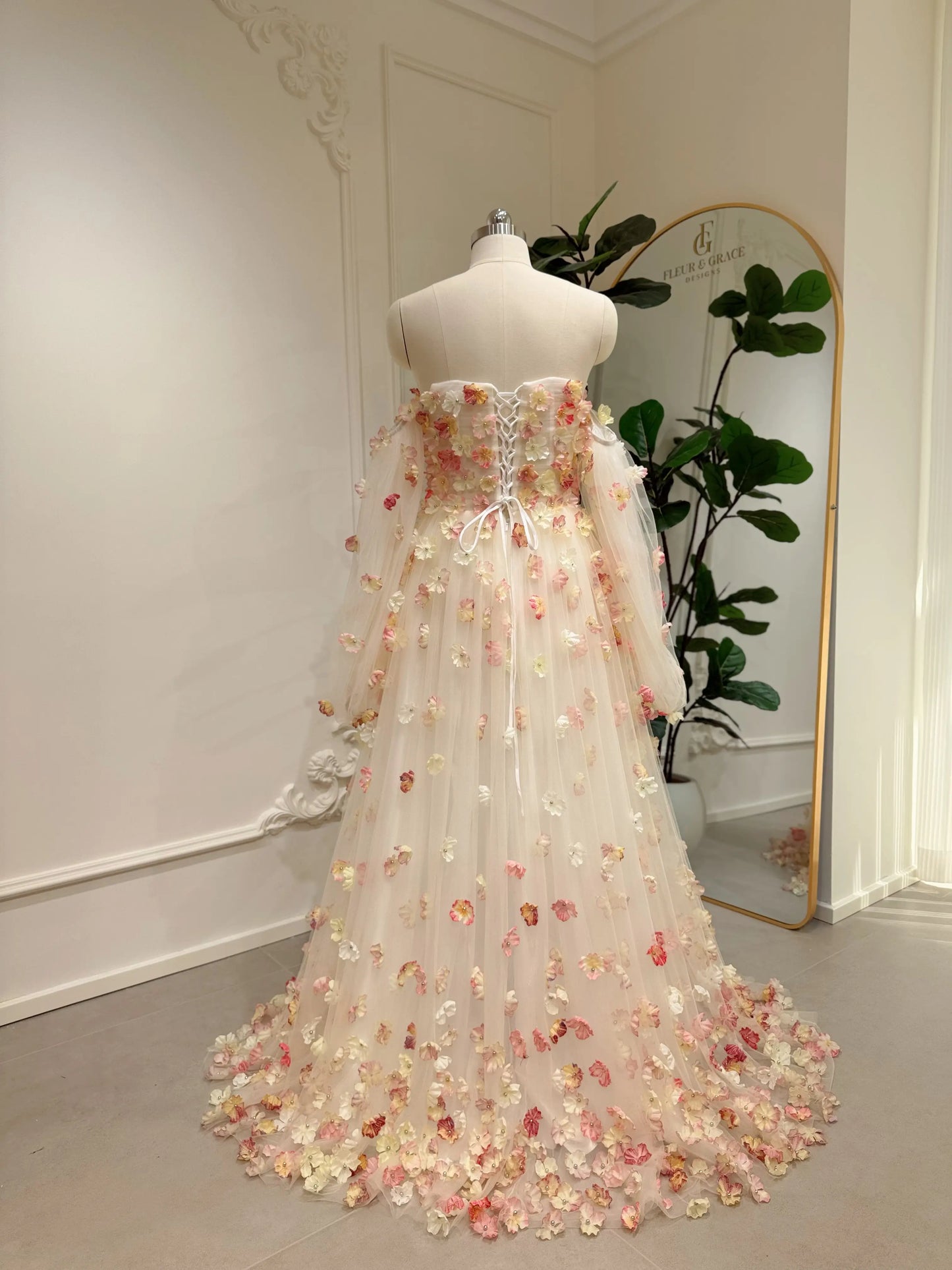 Pink floor-length wedding gown with 3D floral appliqués, removable sleeves, and a lace-up corset back on a mannequin.