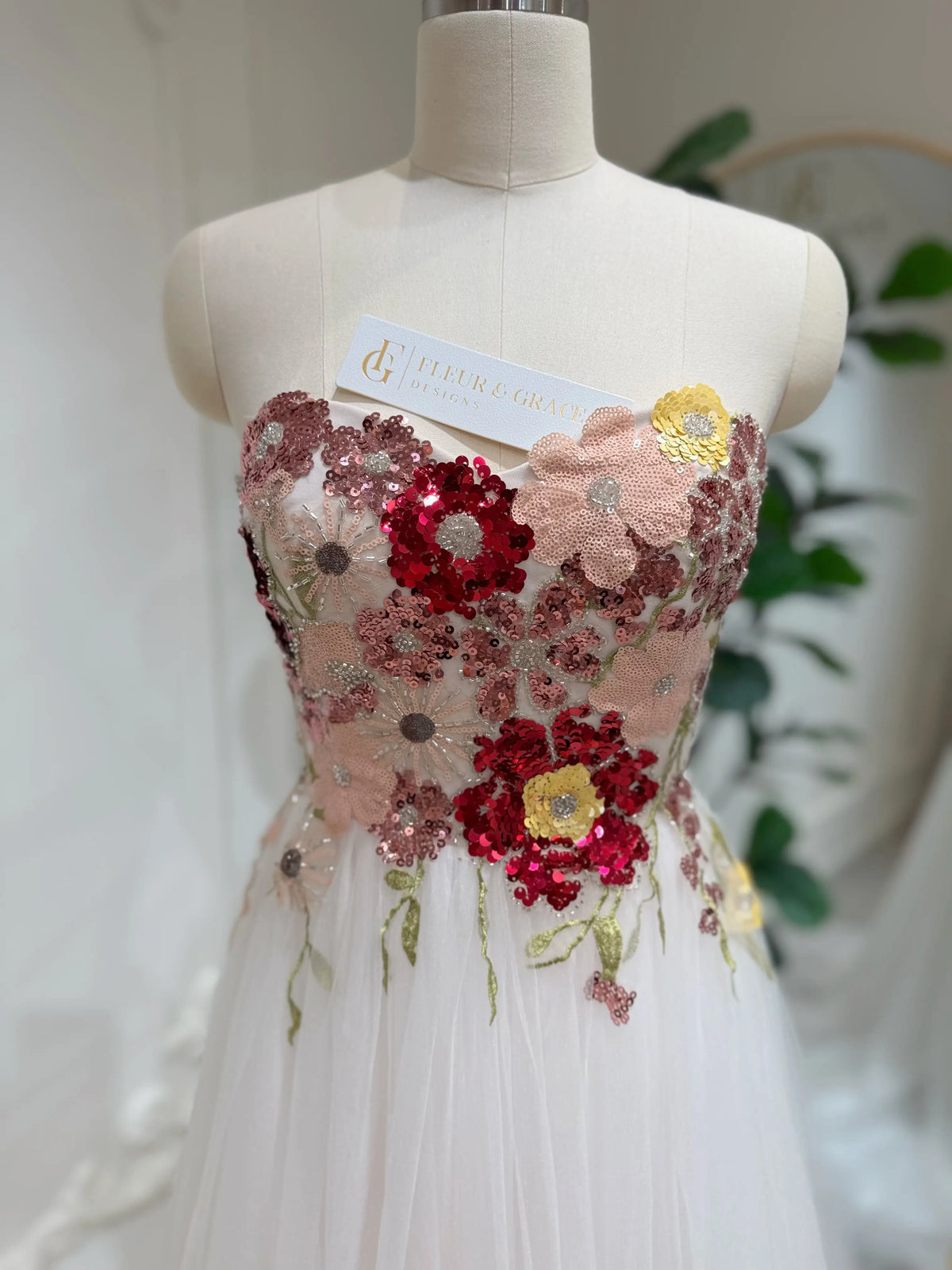 Strapless fairy wedding dress with a colorful sequin floral bodice and blush pink tulle skirt on a mannequin.