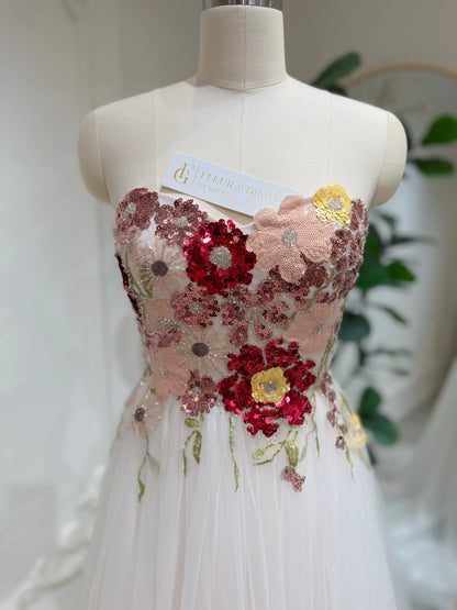 Strapless fairy wedding dress with a colorful sequin floral bodice and blush pink tulle skirt on a mannequin.