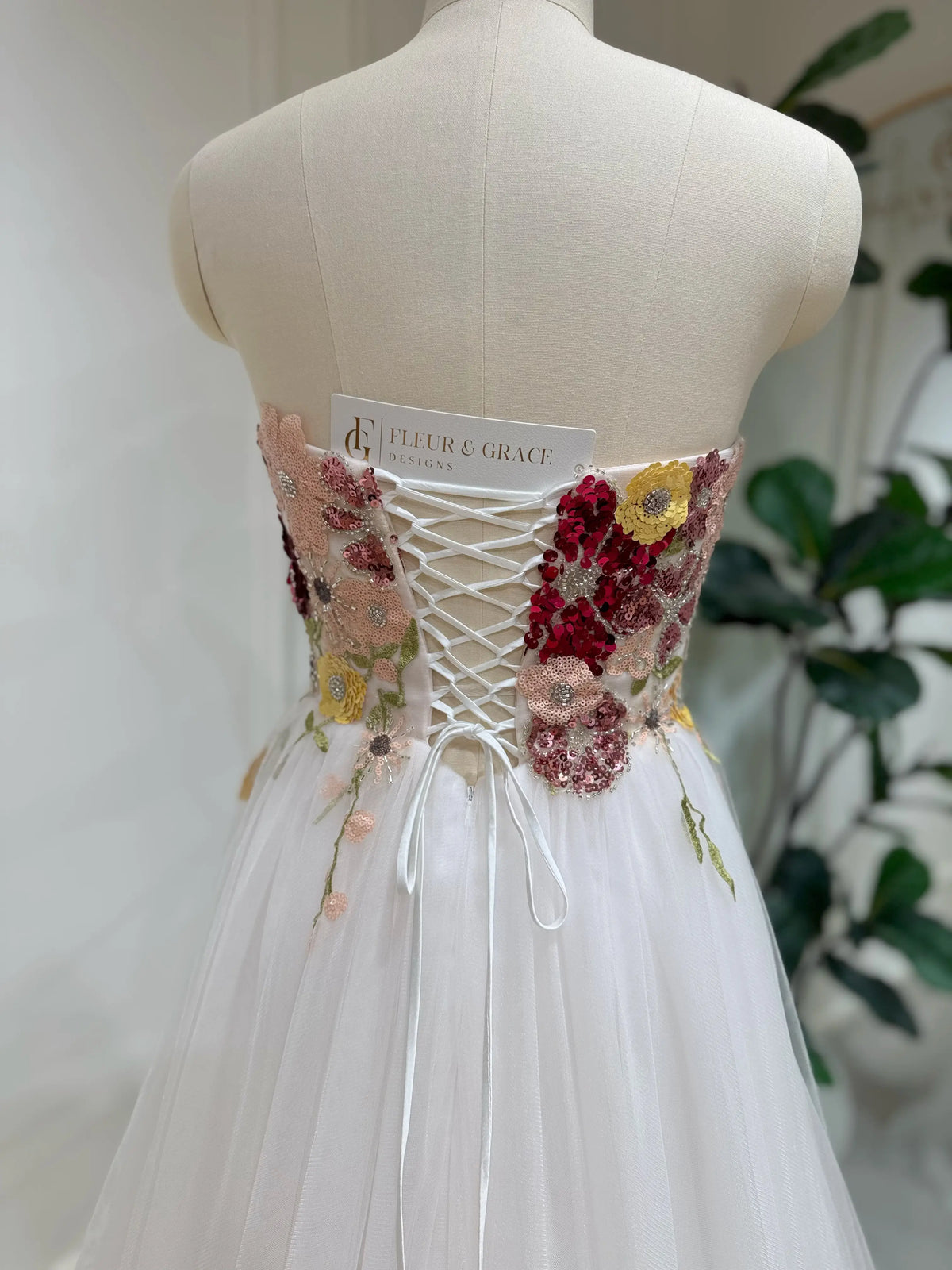 Strapless fairy wedding dress with a colorful sequin floral bodice and white lace-up corset back on a mannequin.