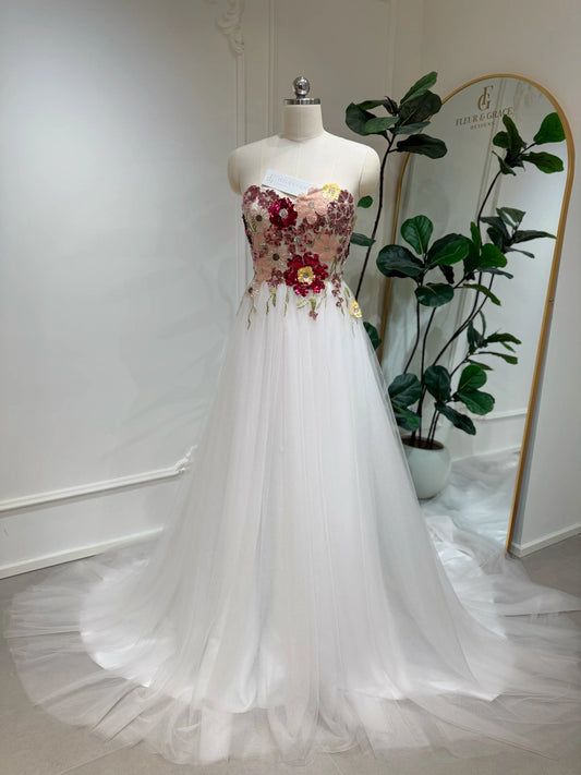 Strapless fairy wedding dress with a colorful beaded floral bodice and flowing blush pink tulle chapel-length skirt.