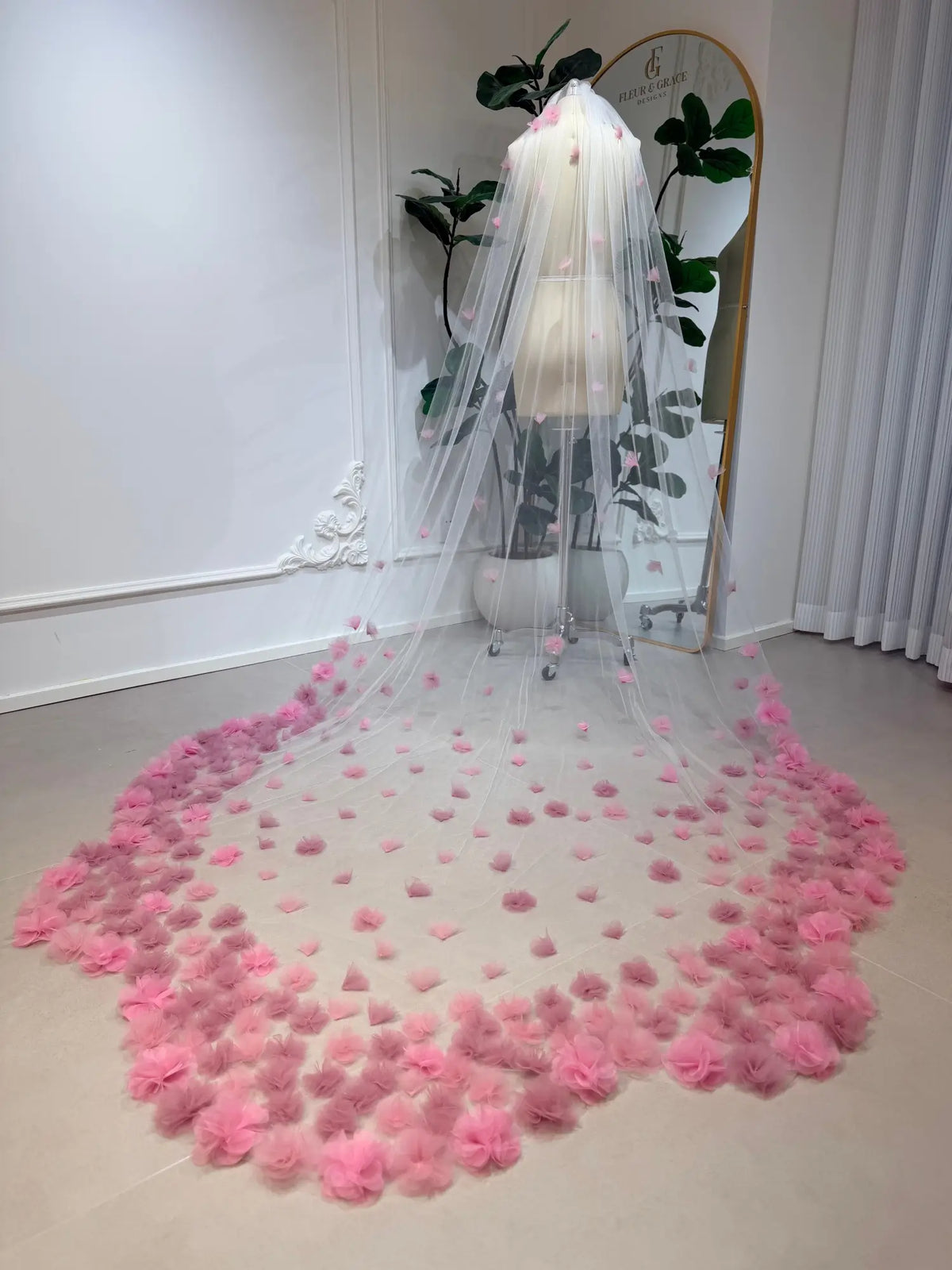 Cathedral-length illusion tulle wedding veil adorned with handmade blush pink 3D flowers on a bridal mannequin.