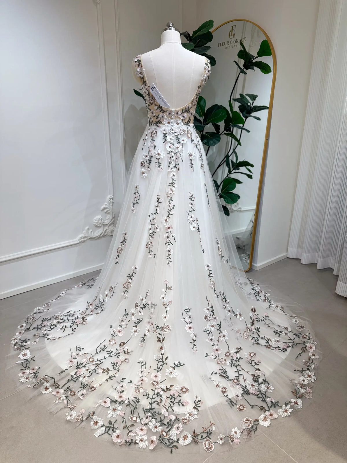 Backless champagne tulle wedding gown with colorful floral embroidery and a flowing chapel-length train on a mannequin.