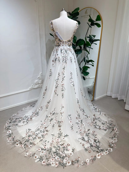 Backless champagne tulle wedding gown with colorful floral embroidery and a flowing chapel-length train on a mannequin.