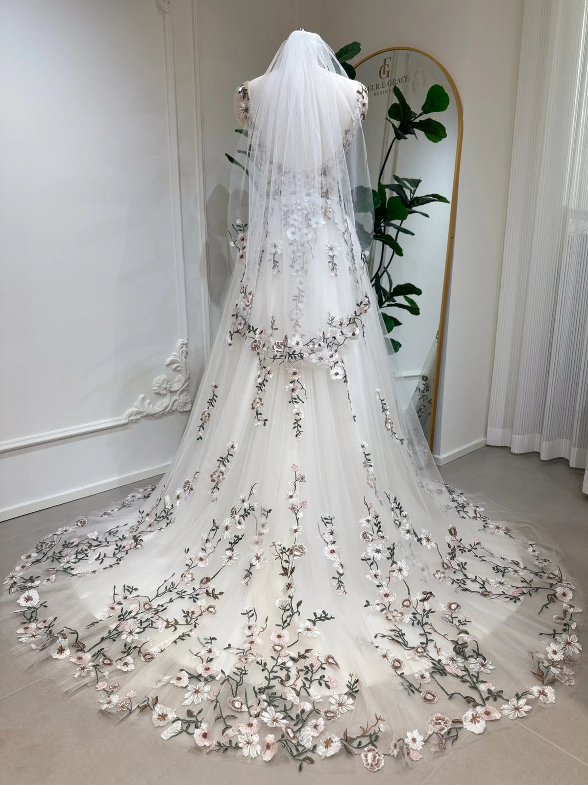Champagne tulle wedding gown with colorful floral embroidery, backless bodice, and a flowing chapel-length train with veil.