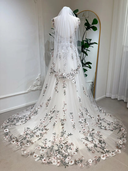 Champagne tulle wedding gown with colorful floral embroidery, backless bodice, and a flowing chapel-length train with veil.