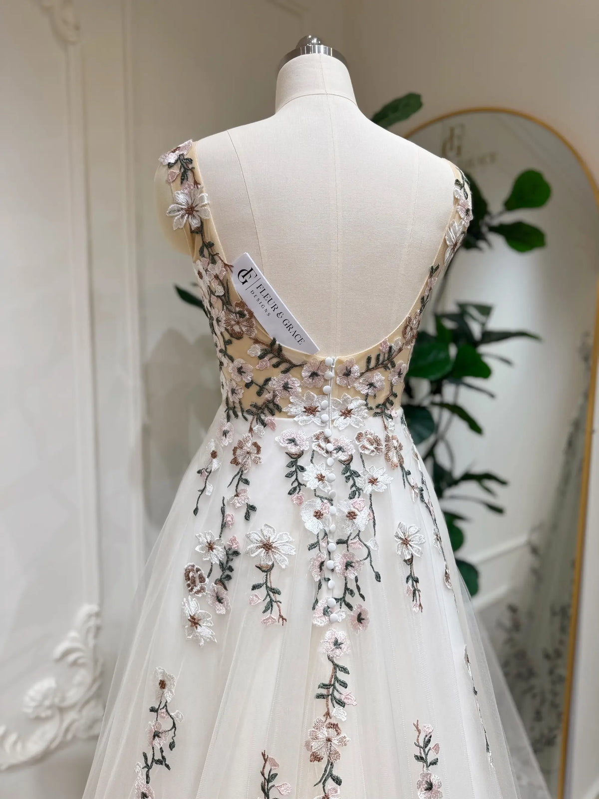 Backless champagne tulle wedding dress featuring delicate multicolored floral embroidery and elegant button-up back detail.