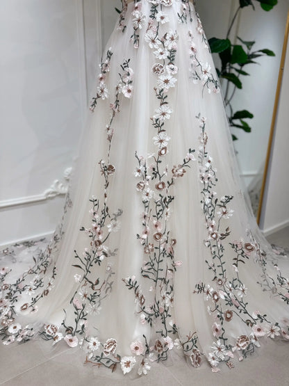 Champagne tulle wedding gown featuring delicate multicolored floral embroidery and a flowing chapel-length train.