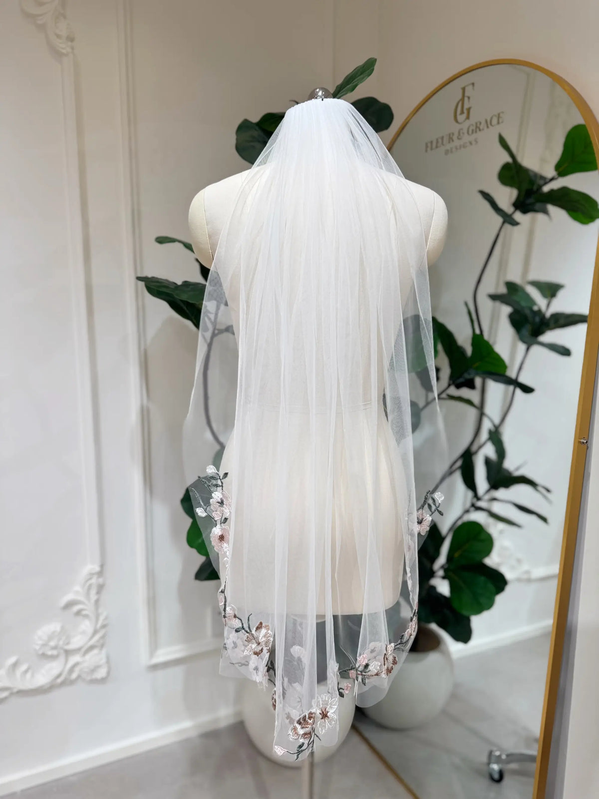 Sheer white bridal veil with delicate multicolored floral embroidery on a mannequin in a boutique setting.