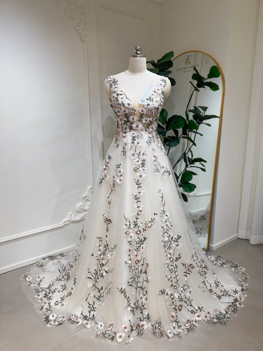 Champagne tulle wedding dress with colorful floral embroidery, sleeveless bodice, and a flowing chapel-length train.