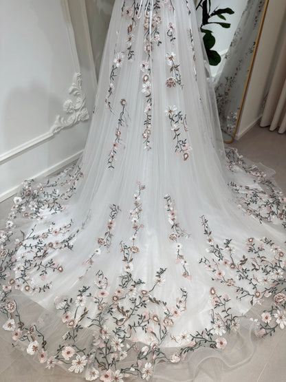 White tulle wedding gown with delicate pink and green floral embroidery and a flowing chapel-length train.