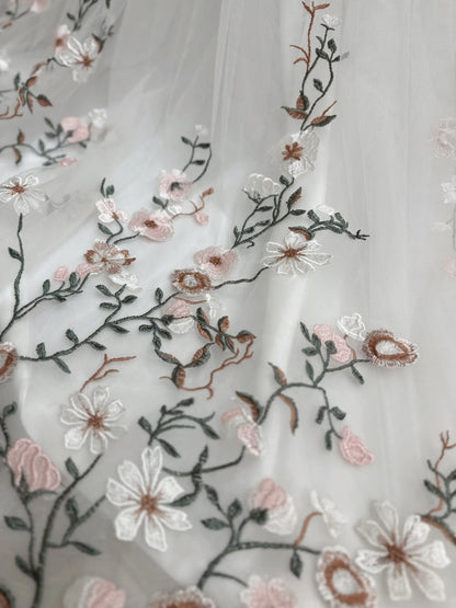White tulle wedding gown fabric featuring delicate pink and green meadow-inspired floral embroidery.