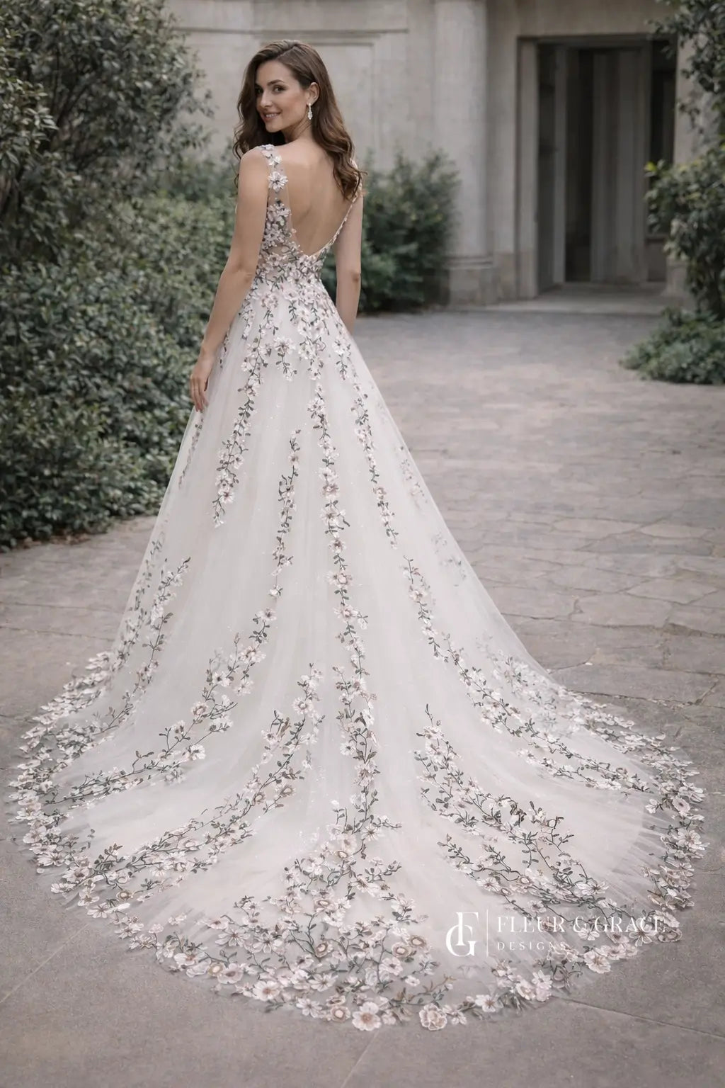 Kate Gown wedding dress with floral embroidery on tulle, V-neckline, and a flowing chapel-length train in a garden setting.