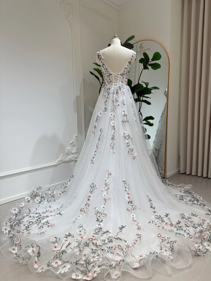 White tulle wedding gown with floral embroidery, lace-up back, and a flowing chapel-length train on a mannequin.