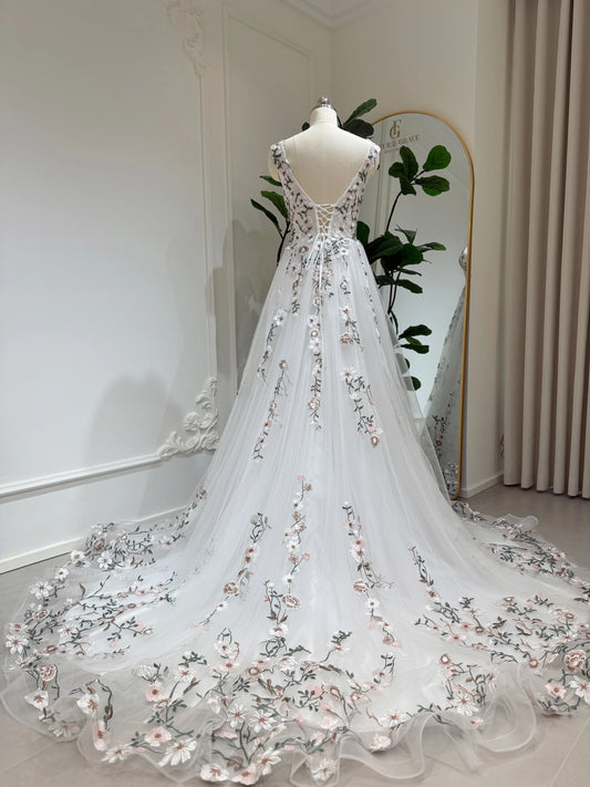 White tulle wedding gown with floral embroidery, lace-up back, and a flowing chapel-length train on a mannequin.