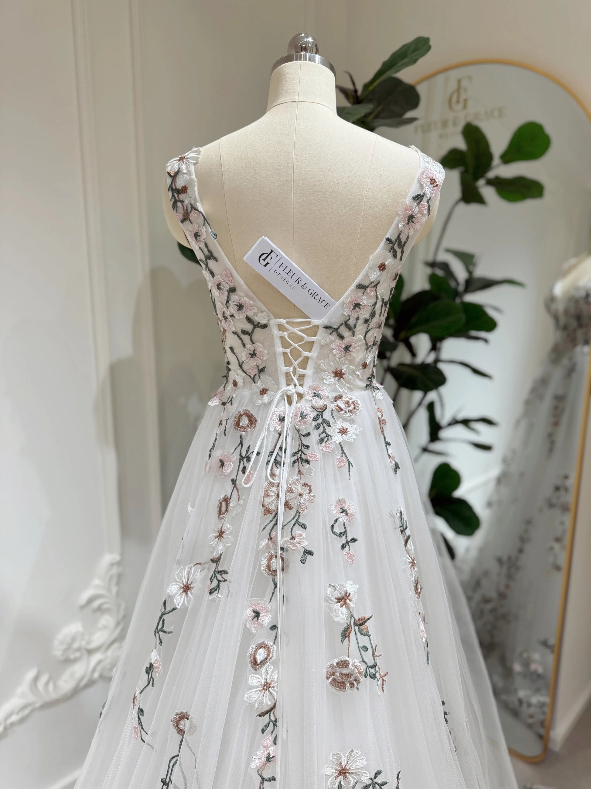 White tulle wedding gown with pink and green floral embroidery, featuring a lace-up back and V-neckline on a mannequin.