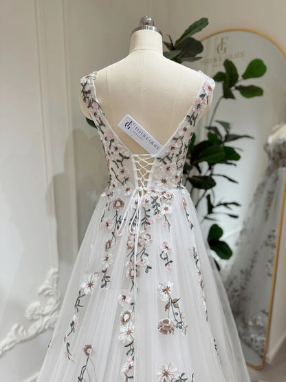 White tulle wedding gown with pink and green floral embroidery, featuring a lace-up back and V-neckline on a mannequin.