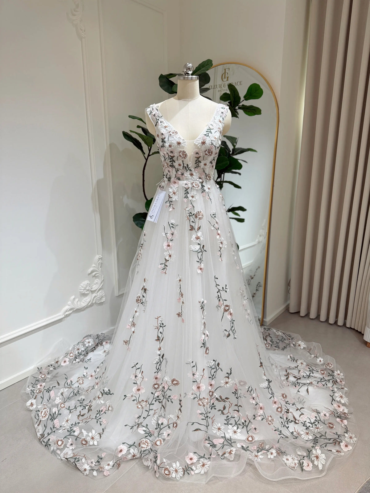 Kate Gown wedding dress with floral embroidery on tulle, V-neckline, and a flowing chapel-length train on a mannequin.