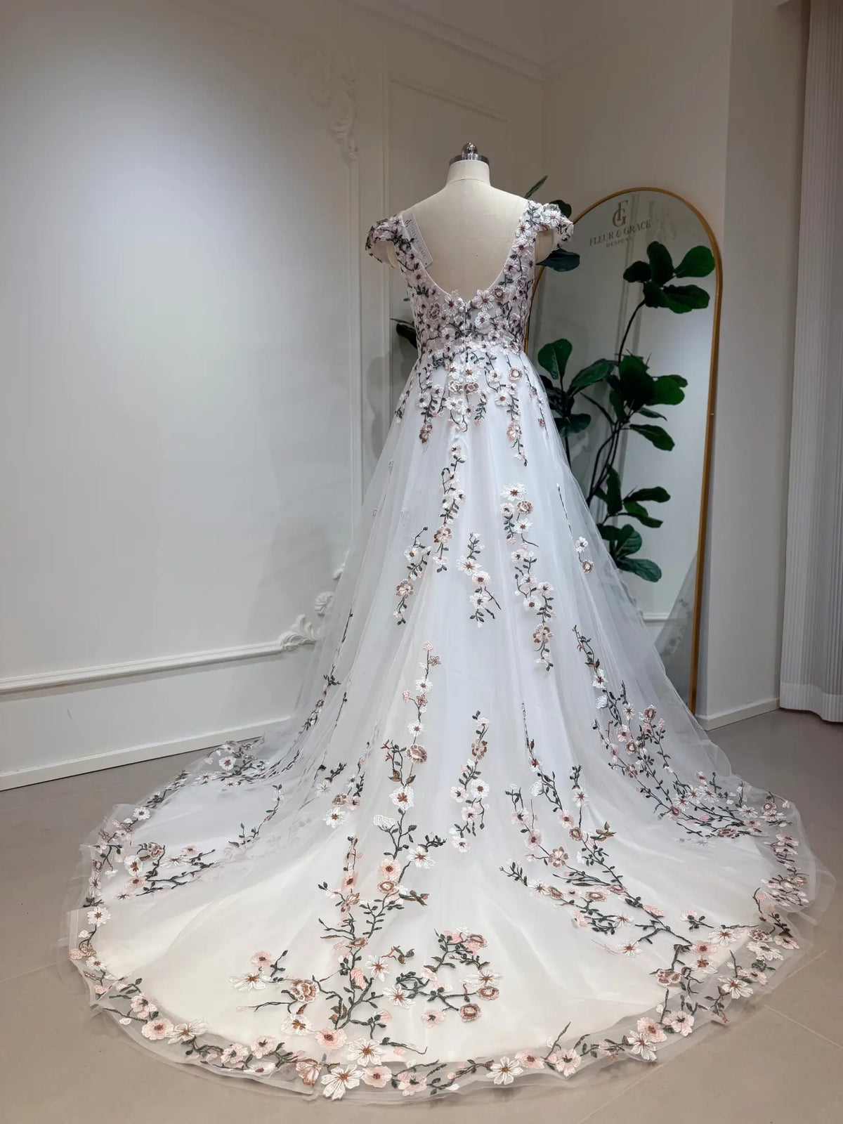A-line wedding dress with cap sleeves, 3D floral embroidery, and a flowing tulle chapel train on a mannequin.