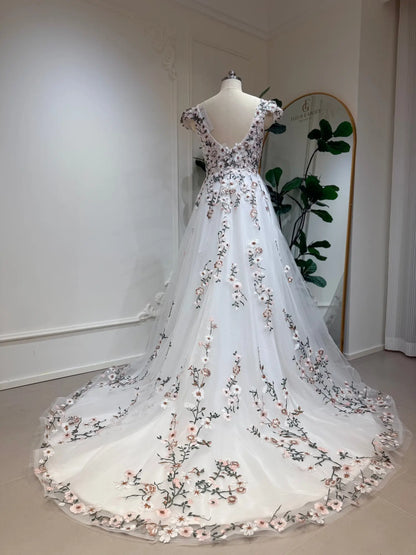 A-line wedding dress with cap sleeves, 3D floral embroidery, and a flowing tulle chapel train on a mannequin.