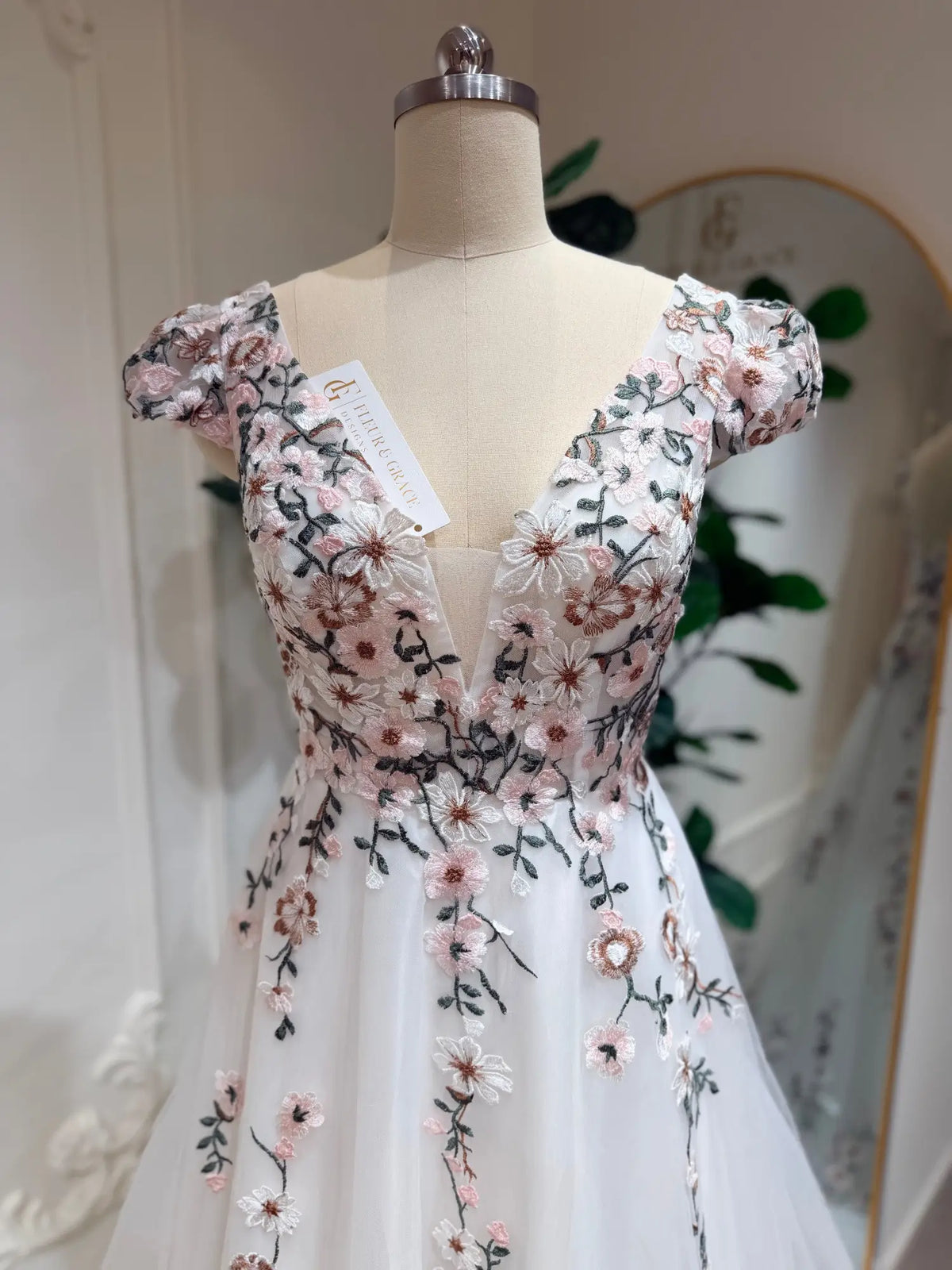 White A-line wedding dress with cap sleeves, deep V-neck, and pink 3D floral embroidery on tulle.