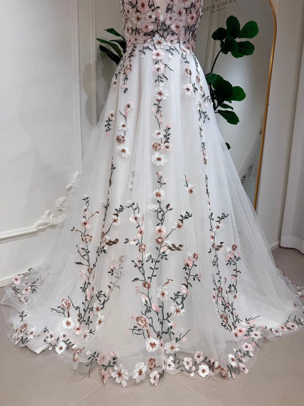 A-line wedding dress in white tulle with delicate 3D pink floral embroidery and botanical vine details.